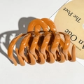 Detailed top view of large caramel orange hair claw clip on white leather background - Orange