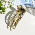 Detail view of the marble-textured resin four-prong hair clip on white leather - Coffee & Black