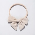 Detail of baby headband featuring textured oatmeal fabric bow on soft nylon elastic band - Beige