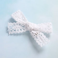 Dettaglio del fiocco in pizzo bianco con motivi all'uncinetto e fermaglio metallico sul retro - Stile Geometrico Fine / Bianco