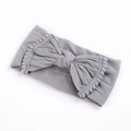 Detail of grey elastic baby headband featuring a large bow and pom-pom tassel edges - Gray