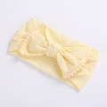 Close-up of soft cream yellow baby headband with pom-pom trim and central bow design - Beige