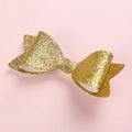 Primo piano di un fiocco per capelli con paillettes dorate su sfondo rosa chiaro - Color Oro Chiaro