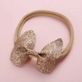 Dettaglio del fiocco a farfalla glitterato oro champagne su fascia elastica per neonati - Oro Scuro