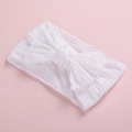 Close-up of white knitted baby headband with a cable stitch texture and large bow detail - White
