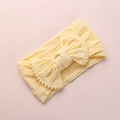 Détail d'un bandeau bébé jaune clair avec nœud jacquard et bordure à pompons - Beige