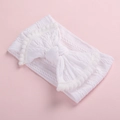 Détail macro du bandeau bébé blanc en tricot torsadé avec un nœud et des pompons - Blanc