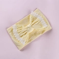 Détail d'un bandeau bébé jaune avec des bords en dentelle et un grand nœud décoratif - Beige