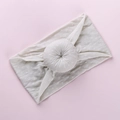 Detail of soft cream knitted baby headband featuring a textured donut knot on pink background - Off-White