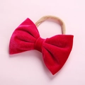 Red velvet baby bow headband with seamless nude nylon band on a soft pink background - Red