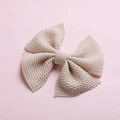 Detail of a large beige bow hair clip with textured honeycomb waffle fabric on pink background - Off-White