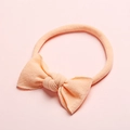 Gros plan d'un bandeau pour bébé en nylon rose doux avec un nœud et un tissu en maille texturé - Orange clair