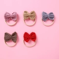 Close-up of five colorful knitted bow headbands for babies on a soft pink background - Random Color