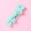 Gros plan sur la texture gaufrée vert menthe d'un bandeau pour bébé avec nœud sur fond rose - Vert menthe