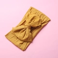 Detailed texture of mustard yellow nylon bow headband for babies on pink background - Turmeric