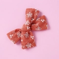 Detail of a brick red cotton lace hair bow clip featuring white floral embroidery art - Orange Red