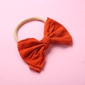 Détail d'un bandeau en nylon pour bébé avec un grand nœud rouge orangé sur fond rose - Rouge Orangé