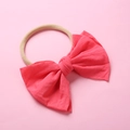 Vue détaillée du bandeau pour bébé en nylon avec nœud en tissu rose corail sur fond rose - 20 Rouge Pastèque