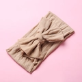 Detail of a soft beige nylon headband with a large bow for infants on a pink background - Nude