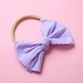 Détail d'un bandeau en nylon pour bébé avec un grand nœud lilas sur fond rose - Violet