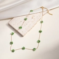 Elegant gold necklace with green beaded flowers on a textured stone and silk background - Green (25436)