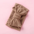 Detailed texture of light brown ribbed knit fabric with a large oversized bow on headband - Nude