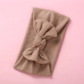 Brown ribbed knit baby headband with a large bow on a soft pink background - Nude
