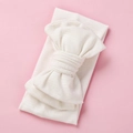 Detail of soft ribbed white baby headband featuring a large oversized knit bow - White