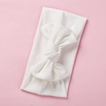 Close-up of white ribbed knit baby headband featuring a large elastic cotton bow - White
