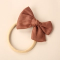 Detailed macro view of dark brown linen bow knot on a soft beige elastic baby headband - Orange