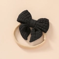 Detailed macro view of black waffle texture bow on soft beige nylon baby headband - Solid Black