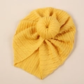 Detail of yellow cable knit baby turban hat featuring a large donut knot decoration - Ginger Yellow