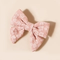 Dettaglio del fermaglio a fiocco in pizzo rosa con trama floreale in rilievo e toni caldi - 7.7*7.1cm / Rosa