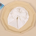Close-up of white velvet baby turban hat with oversized bow on a textured display tray - White