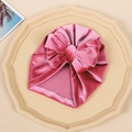 Pink velvet baby turban hat with a large bow displayed on a tray for infants - Peach Pink