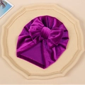 Detailed close-up of a purple velvet baby turban hat with a large golden bow decoration - Fuschia