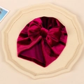 Detail of baby velvet hat in deep wine red featuring a large decorative golden velvet bow - Brick Red