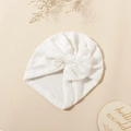 Detailed texture of white ribbed baby turban hat with a bow on cream background - White