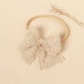Dettaglio della fascia per neonati in pizzo con fiocco su sfondo beige delicato - Bianco Sporco
