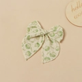 Dettaglio del fermaglio a fiocco in cotone floreale per neonati su sfondo di legno naturale - Fiore verde