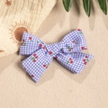 Close-up of blue plaid bow hair clip with red cherry prints on a summer textured background - Blue and Purple