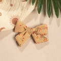 Detail of gingham bow hair accessory with cherry print on beige sand background - Turmeric