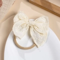 Close-up of cream embroidered cotton bow headband with soft nylon strap on ceramic plate - Off White