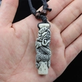 Detail view of a resin dragon totem pendant held in hand with black woven cord - White