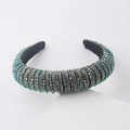 Detail of wide padded headband with green crystals and gold beads on white stone pedestal - Green Crystal Beaded Style
