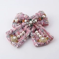 Dettaglio di un fermaglio a fiocco in tweed rosa con perle e strass su sfondo bianco - Fermaglio per Capelli Fiocco Rosa (I)