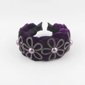 Gros plan d'un serre-tête en velours violet avec motifs floraux en strass et perle centrale - Style Velours Strass Perle / Violet