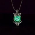 Detailed macro view of silver owl pendant glowing green in dark environment - Green