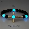Macro di perle blu luminose e croce dorata su bracciale di pietra lavica nera - Oro Antico Luce Blu