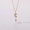 Vista macro del collar dorado con colgante de luna de nácar y perla blanca redonda - Estilo Luna Perla